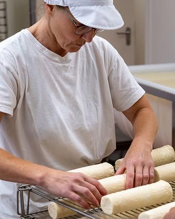 3/3: Dank aan alle nieuwe volgers voor jullie interesse in ons ambacht. We geven je in drie opeenvolgende berichten graag een inkijk in het productieproces van een van onze meest geliefde en bekroonde kazen: Aurélie.

👀🧀 Rijpen en inpakken

Aurélie is nu stevig genoeg om van het netje gehaald te worden. De kazen worden stuk per stuk gedraaid en gaan terug de rijping in om verder te drogen en te rijpen. Dat herhalen we elke dag, zodat de kazen gelijkmatig rijpen. Beetje bij beetje ontwikkelt ons Aurélie haar mooie geotricumkorstje. Elke dag checken we de temperatuur, luchtvochtigheid en luchtcirculatie in de rijping. Aan het einde van het rijpingsproces heeft Aurélie een mooie, lichtgele korst gekregen. We wegen en labelen de kazen, waarna ze in een kartonnen doos met voldoende verluchtingsgaten worden verpakt. Aurélie is zacht van smaak en wint bij het ouder worden aan karakter en smaakrijkdom.