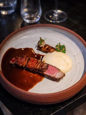 Dans ces assiettes, un bœuf Holstein de 37 mois.
Élevé trois saisons en pâture, puis engraissé quelques semaines avec les vaches de la « Bou cherie Originelle » à Emines.

Il y a 3 ans, les veaux laitiers ne valaient plus rien.
Alors Sébastien et Benjamin Geens ont fait un pari : élever des bœufs Holstein, une voie peu explorée dans la filière laitière.
Avec quelques conseils de leur père (qui faisait déjà ça en 1970)… et beaucoup d’instinct.

Stefan a fait le choix fort : commander l’animal entier.
Pour sécuriser les éleveurs. Pour valoriser chaque partie. Pour travailler le produit sur mesure.

Résultat dans l’assiette :
une viande fondante, avec un peu plus de mâche, un gras délicat.

Déclinée en :
— bavette grillée
— tartare dans les morceaux plus gras
— et en point d’orgue : un cannelloni de queue et flanchet

Sans oublier le fond, réalisé avec tous les os.

Ici, rien ne se perd.
Tout se transforme.
Et surtout, tout se respecte.