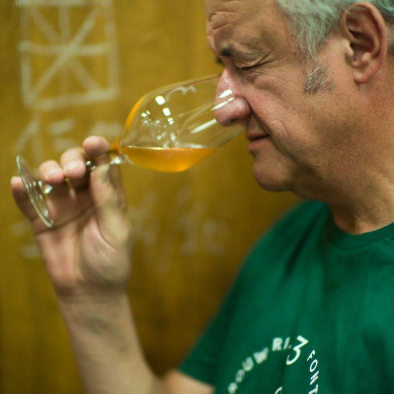 Armand in a green shirt closely examining a glass of beer in front of wooden foeders.