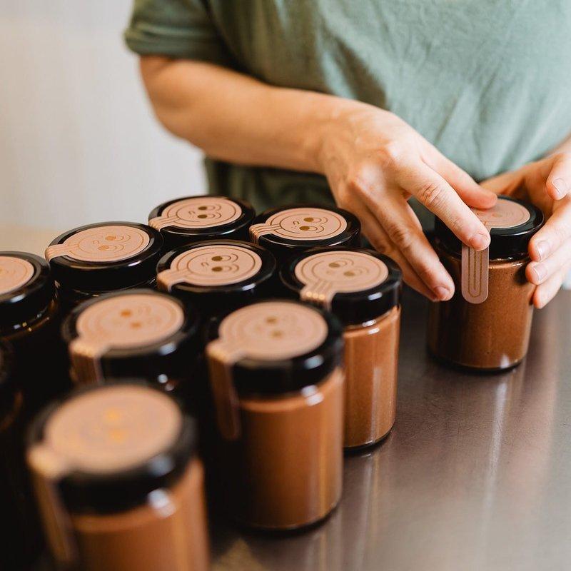 Mains fermant des pots de pâte à tartiner au chocolat à couvercle noir sur un plan de travail en inox.