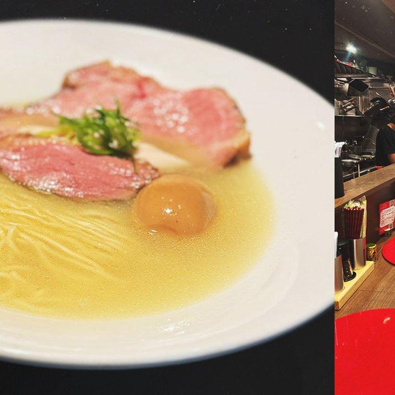 Kom ramen met heldere bouillon, plakjes eend en ei, naast een smalle ramabar met rode onderleggers en krukken